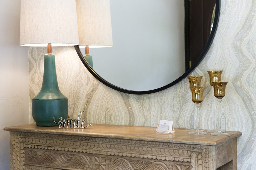 A table with a mirror and lamp. On the table is a sculpture that says 'smile'